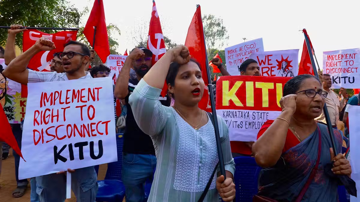 A group of protesters holding banners and flags, with one woman prominently displaying a sign that reads 