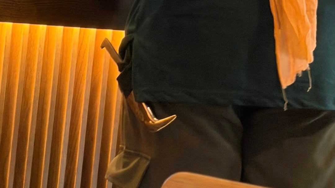 A person wearing a green shirt and an orange scarf stands in front of a counter displaying packaged food items.