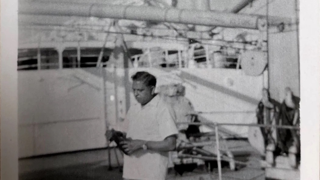 A black and white photograph of a man on a ship, holding a camera, and wearing a watch.