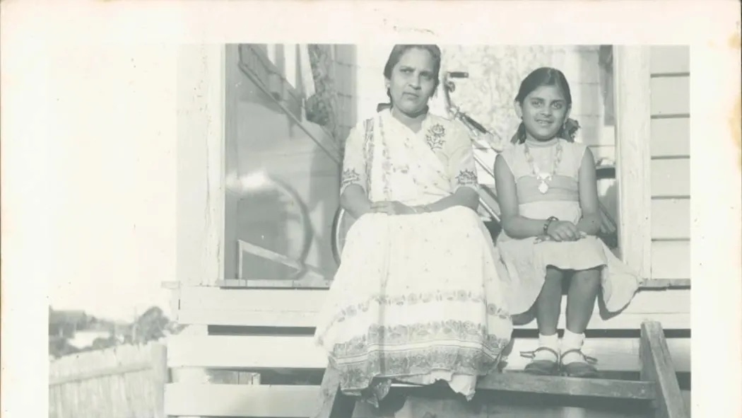A black and white photograph of a woman and a young girl sitting on the steps of a house.