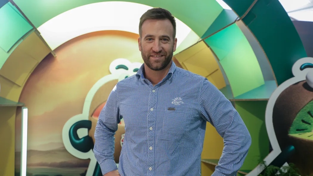 A man stands in front of a colorful, circular backdrop with a smiling face, wearing a blue and white checkered shirt.
