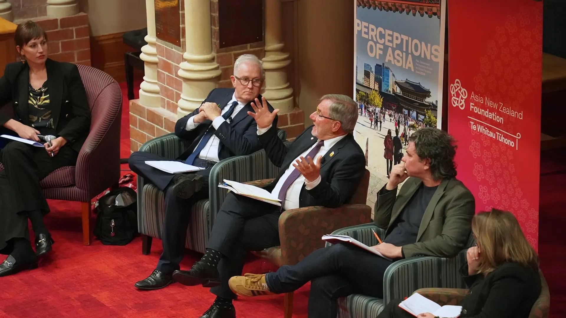 A panel of four individuals, two men and two women, are seated in a formal setting, discussing topics related to Asia as indicated by the backdrop banner titled "Perceptions of Asia."